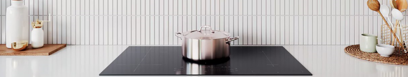 Modern kitchen with a stainless steel pot on a black induction cooktop. On each side there are utensils and jars on a white benchtop.