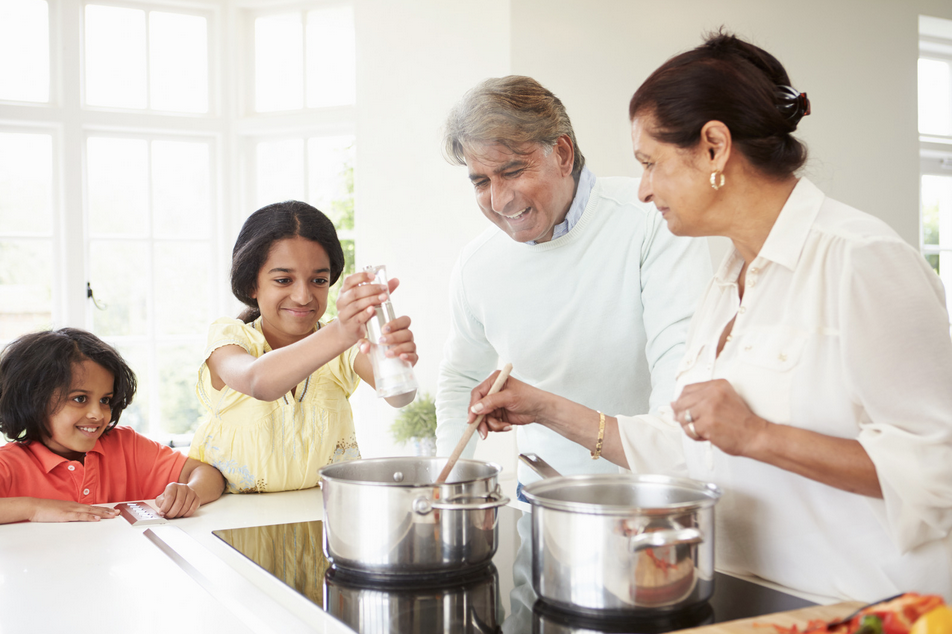 Smiling family cooking together, with two adults and two children. Preparing food on an induction cooktop.